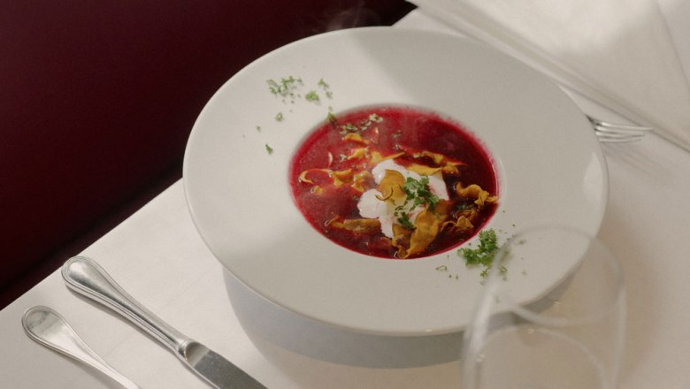 Rote Rüben Suppe, © Niederösterreich Werbung/Julius Hirtzberger Ein Teller mit roter Rübensuppe, garniert mit Sahne und Kräutern, auf einem gedeckten Tisch.