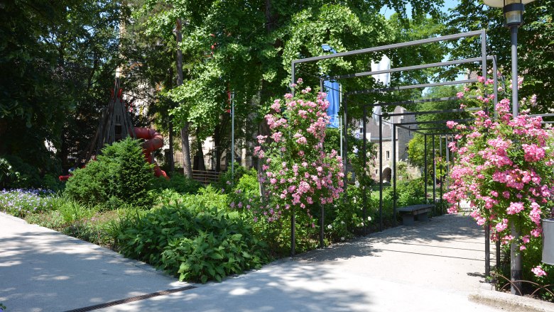 Ein gepflegter Schlosspark mit bl&uuml;henden Rosenb&uuml;schen und einem Spielplatz im Hintergrund.
