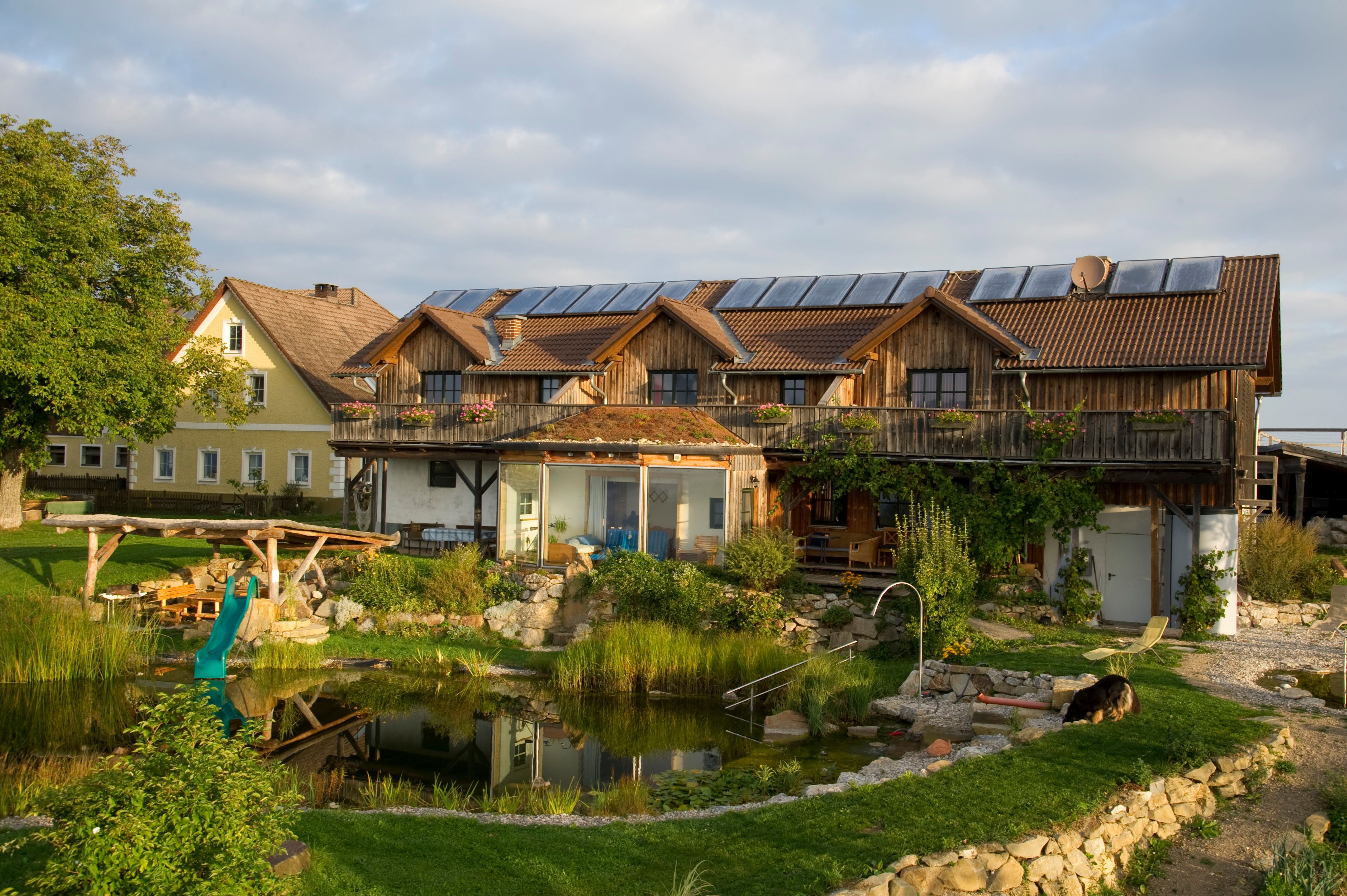 Ein Bio-Bauernhof mit Solarpanelen auf dem Dach, einem Teich und einem Hund im Garten.