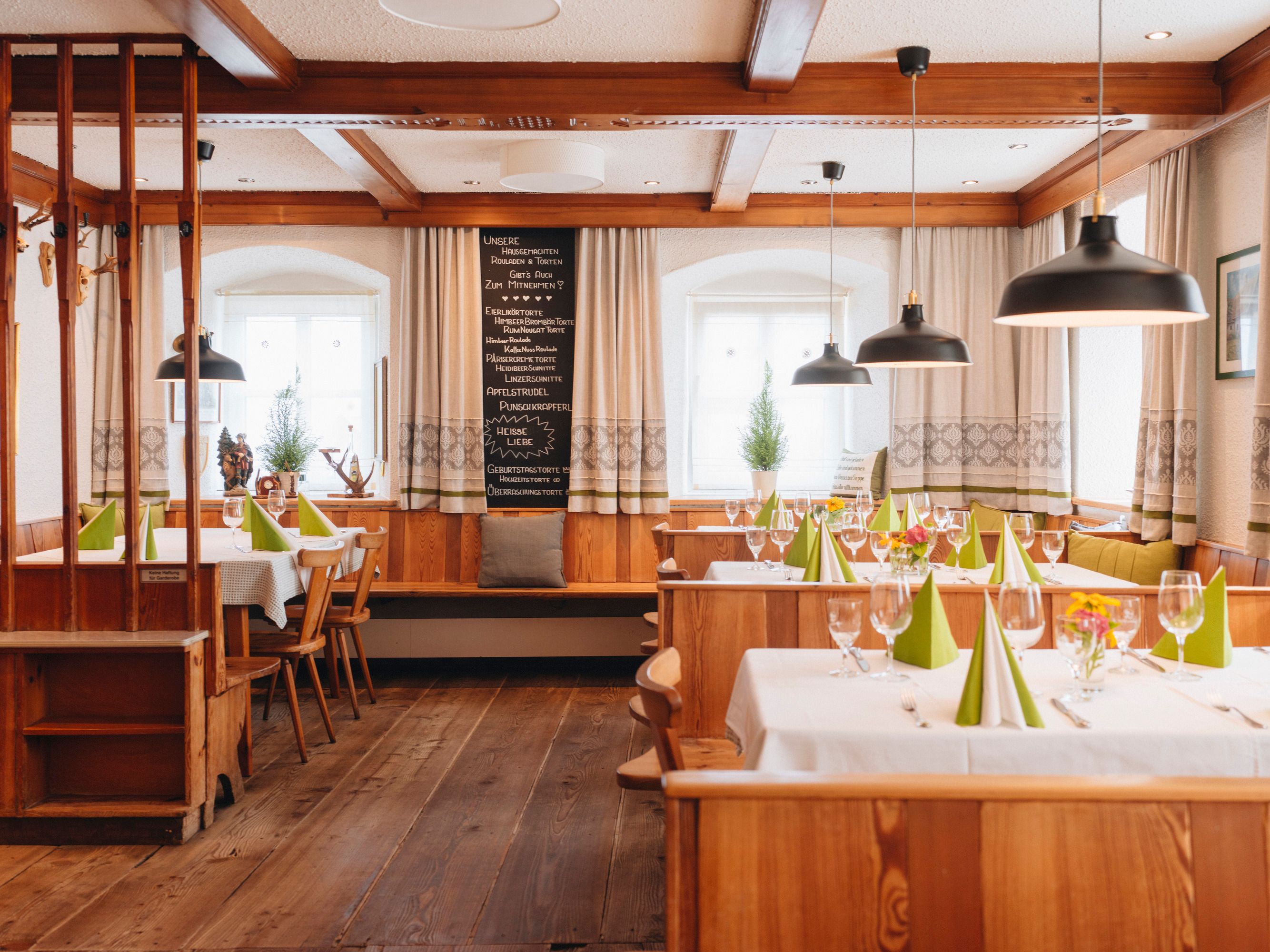 Gemütliche, traditionelle Gaststube mit Holzmöbeln, gedeckten Tischen und grünen Servietten.