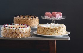 Verschiedene Torten und Gebäck auf einem Tisch vor dunklem Hintergrund.