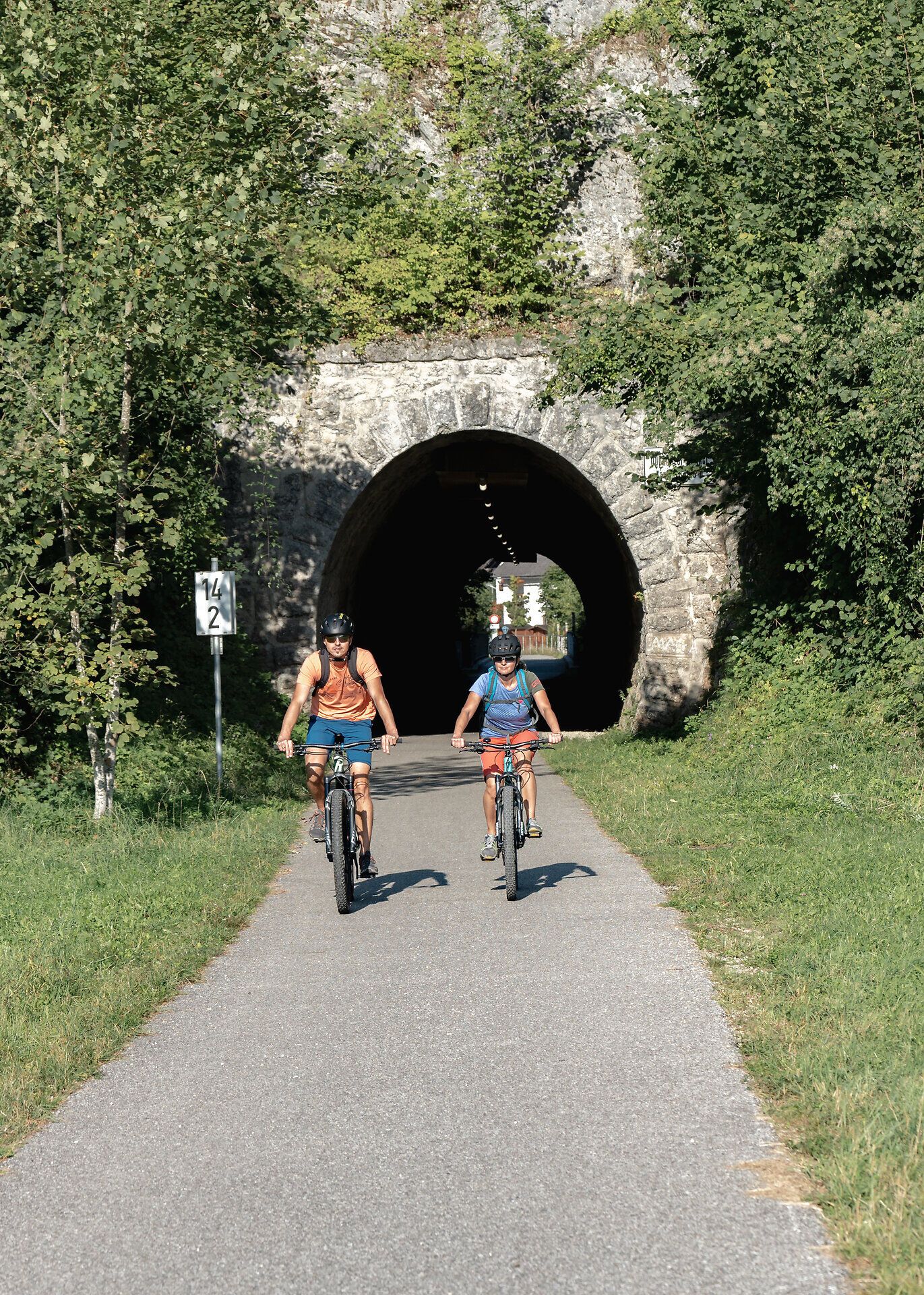 Zwei Radfahrer genießen die frische Luft und die malerische Umgebung der Ybbstaler Alpen, während sie durch einen schattigen Tunnel radeln. Die üppige Vegetation und die sanften Hügel schaffen eine einladende Atmosphäre für Abenteuerlustige und Naturliebhaber.
