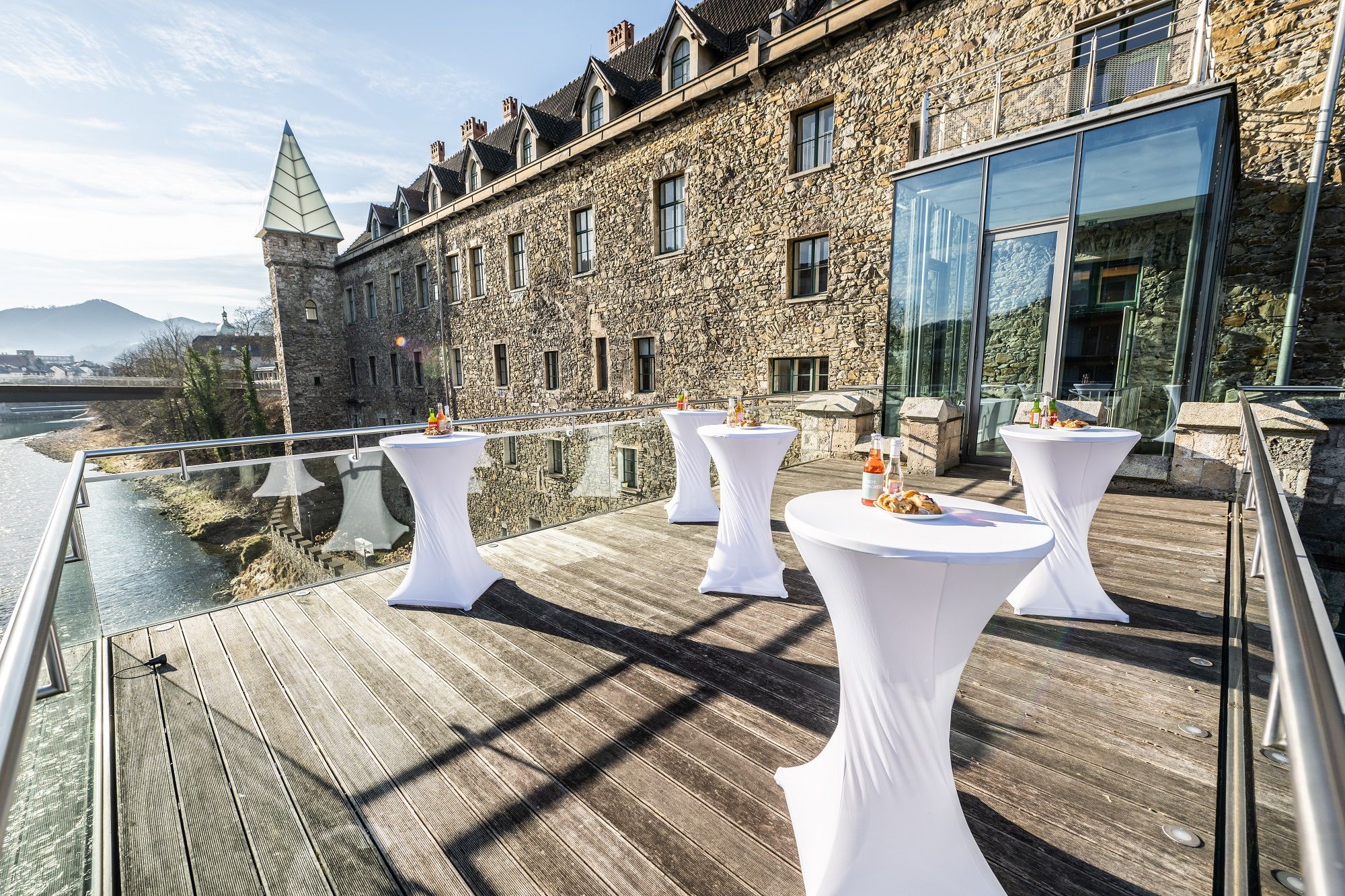 Terrasse mit Stehtischen vor einem historischen Gebäude mit Glasfassade.