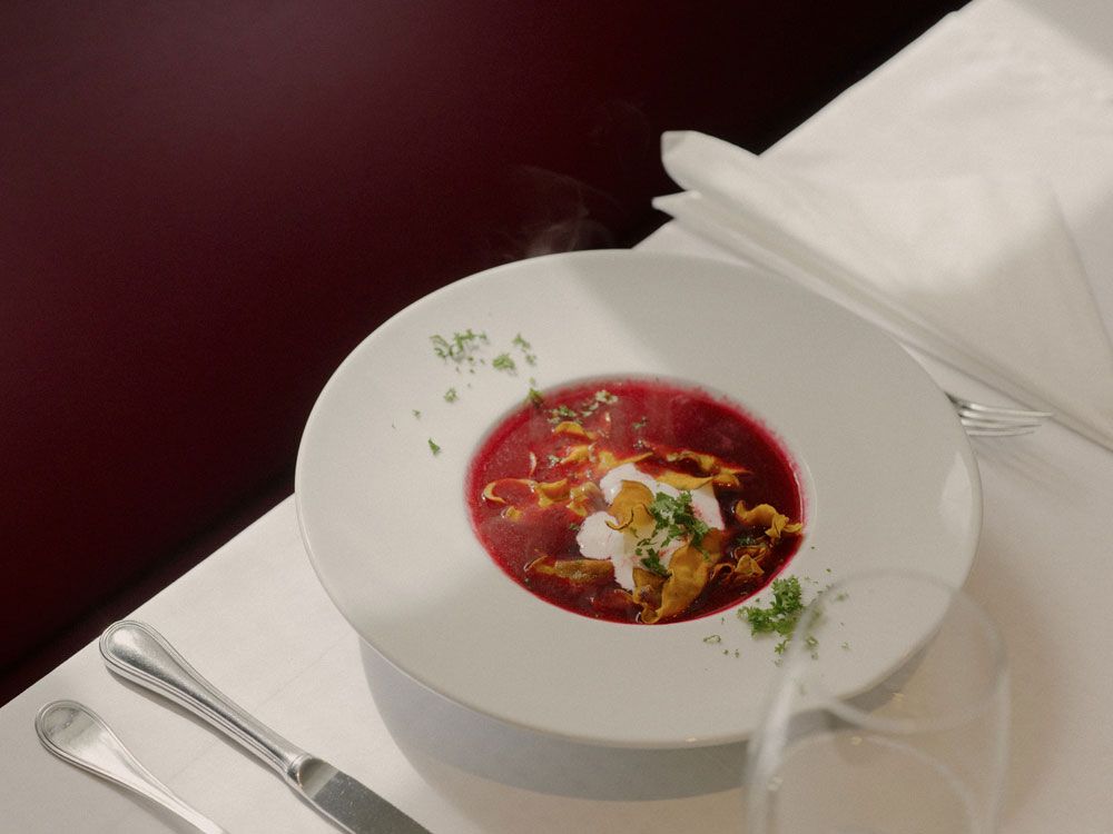 Ein Teller mit roter Rübensuppe, garniert mit Sahne und Kräutern, auf einem gedeckten Tisch.