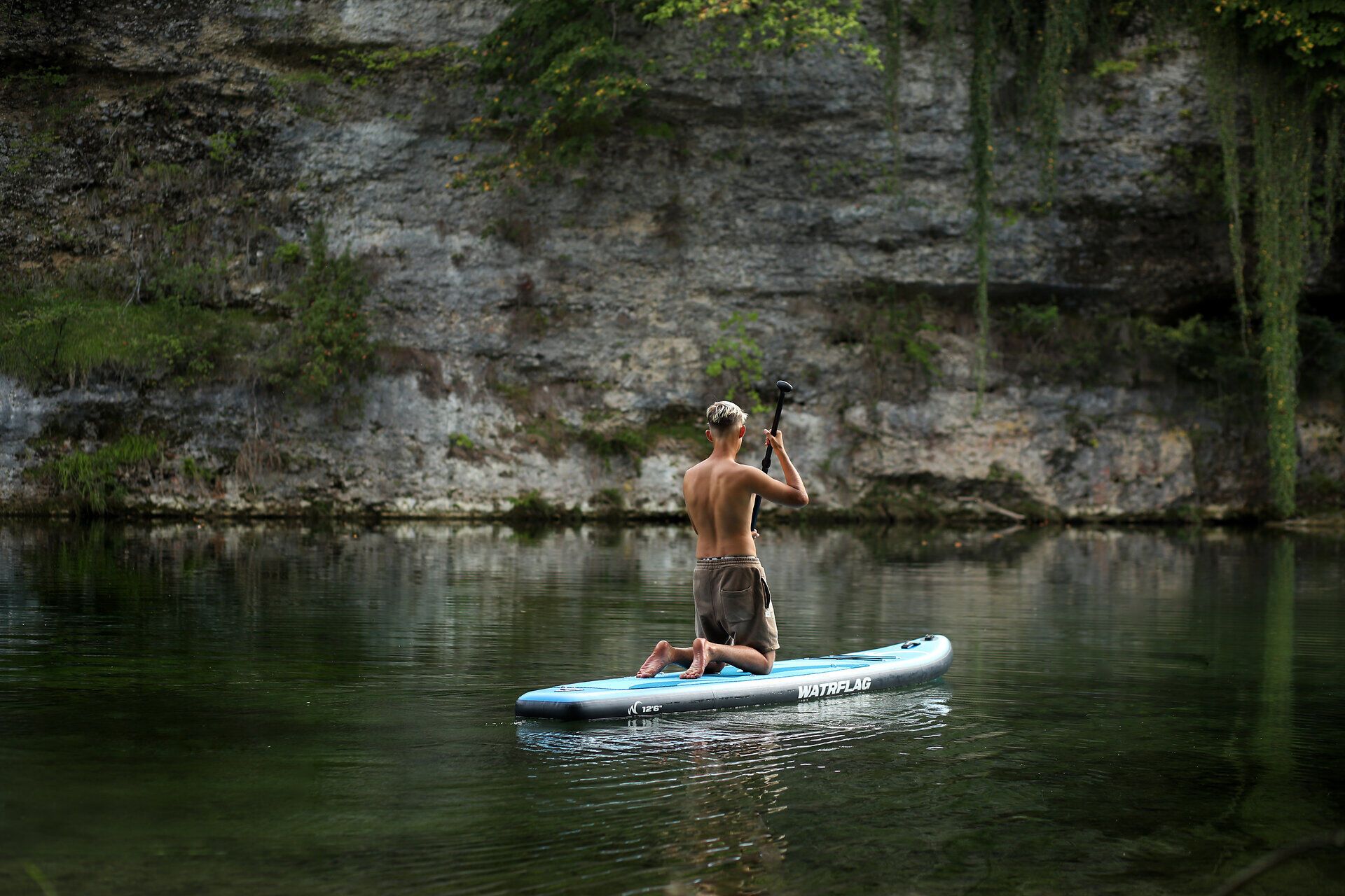 Kind sitzt auf SUP und rudert auf einem Fluss im Naturpark Ybbstal im Mostviertel.