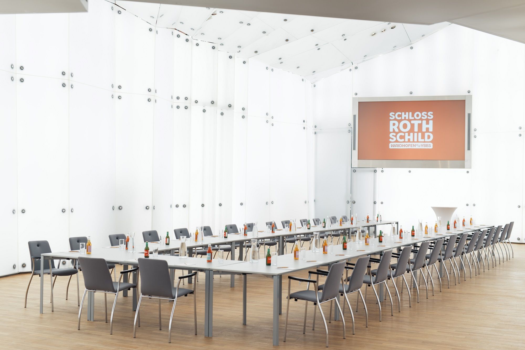 Moderner Konferenzraum im Schloss Rothschild mit langen Tischen, Stühlen und Getränken.