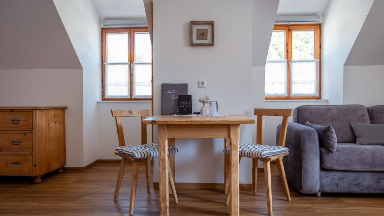 Gem&uuml;tlicher Wohnbereich mit Holztisch, zwei St&uuml;hlen und Sofa.