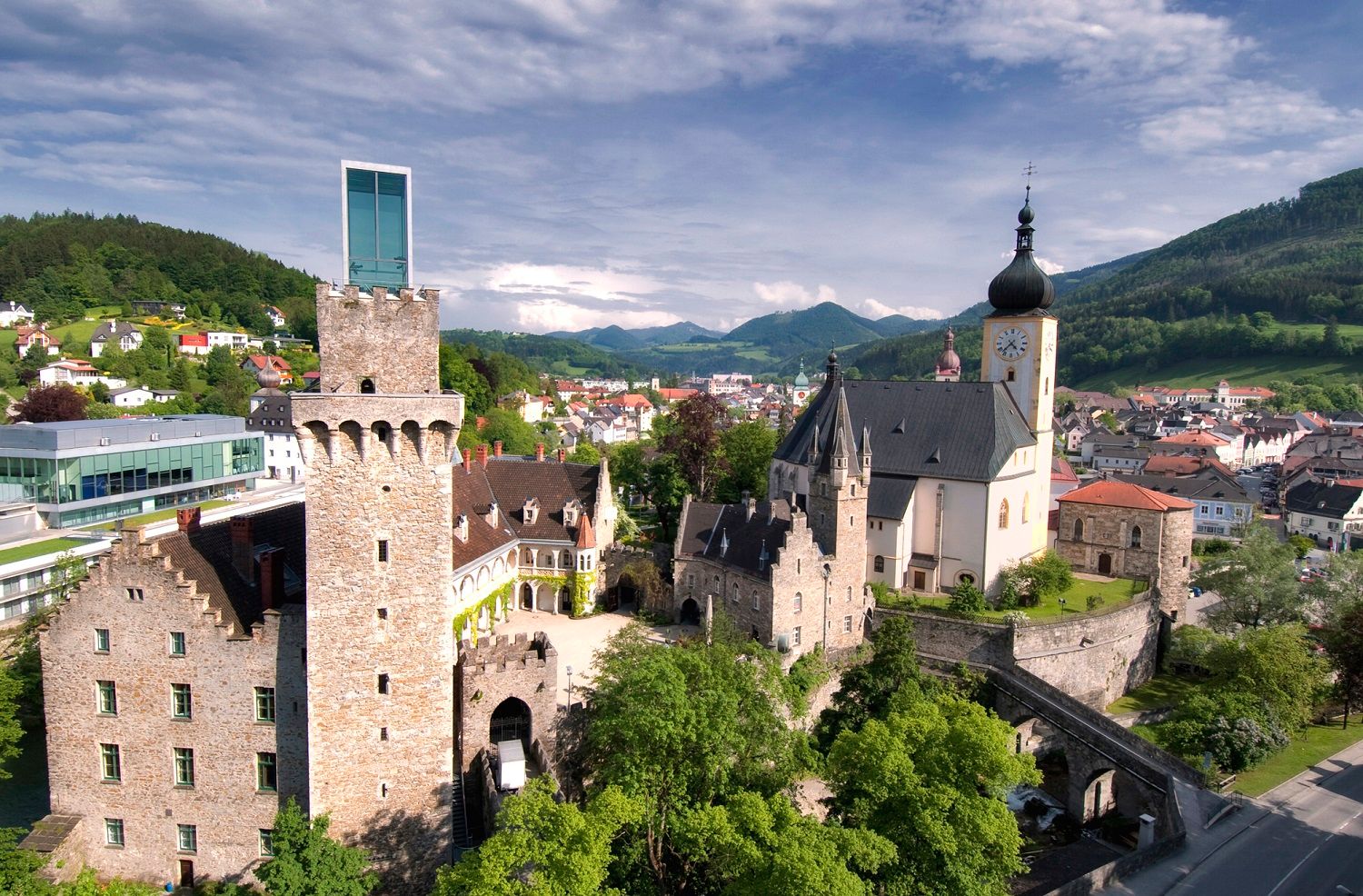 Luftaufnahme von Schloss Rothschild in einer grünen Landschaft mit Bergen im Hintergrund.