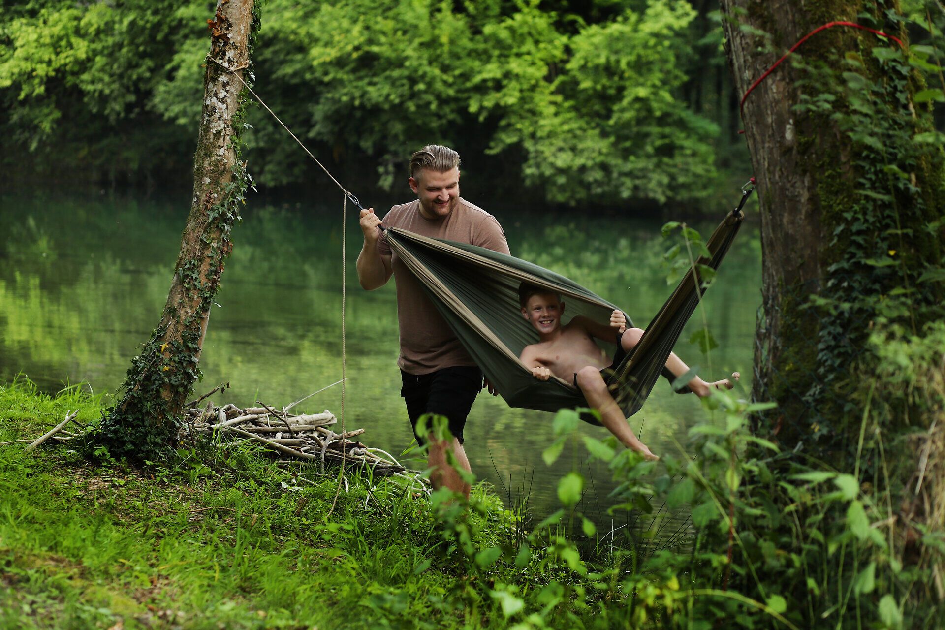 Mann schaukelt Kind in der Hängematte neben einem Fluss im Naturpark Ybbstal im Mostviertel.