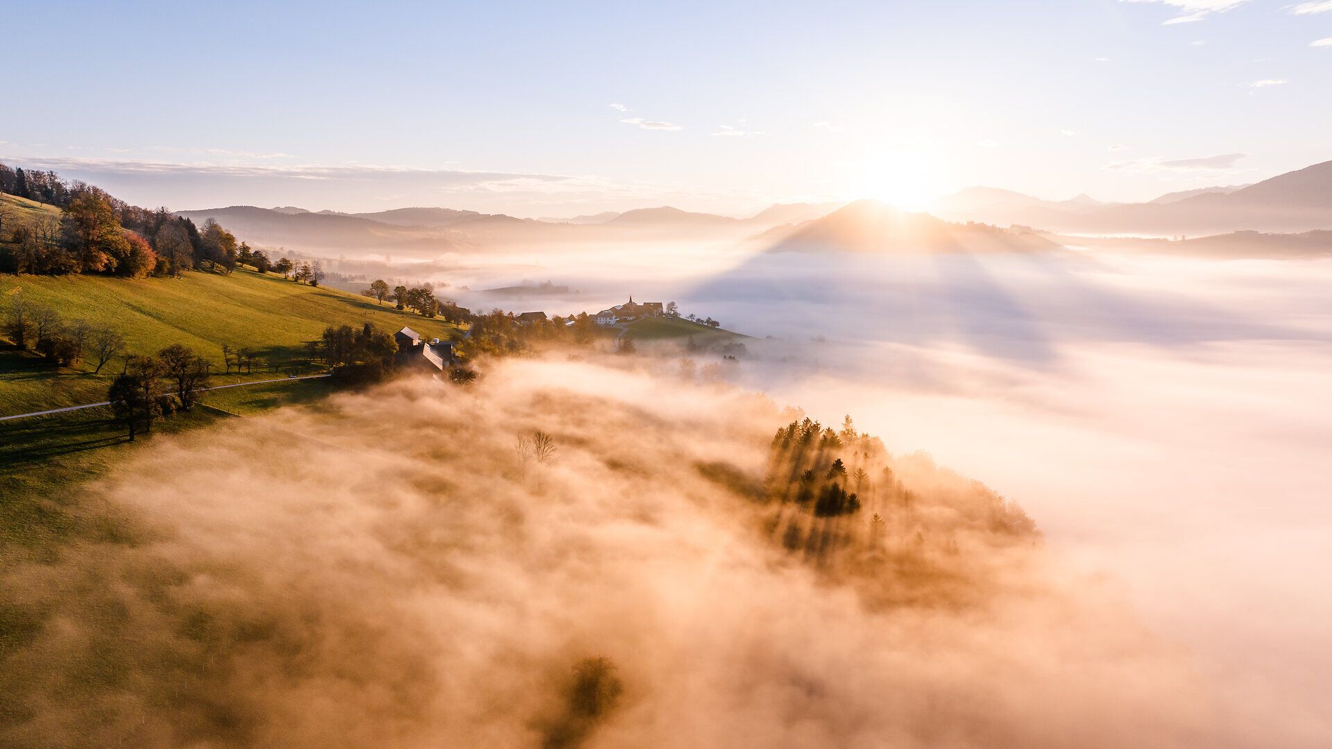 Die sanften Hügel des Mostviertels sind in ein goldenes Licht getaucht, während die Morgensonne über den Nebel aufsteigt. Die malerische Landschaft, durchzogen von saftigem Grün und bunten Herbstblättern, lädt zu unvergesslichen Erlebnissen in der Natur ein.