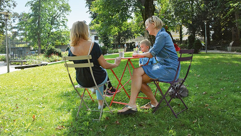 Drei Personen sitzen an einem Tisch im Schlosspark Schloss Rothschild.