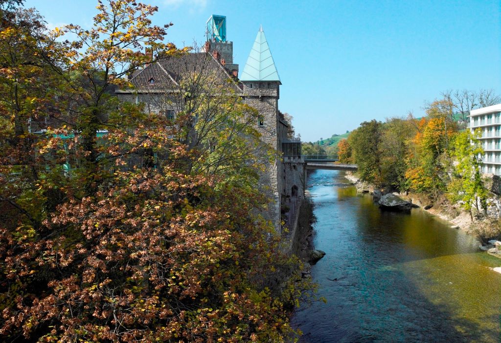 Fluss mit Herbstbäumen und Gebäude im Hintergrund.
