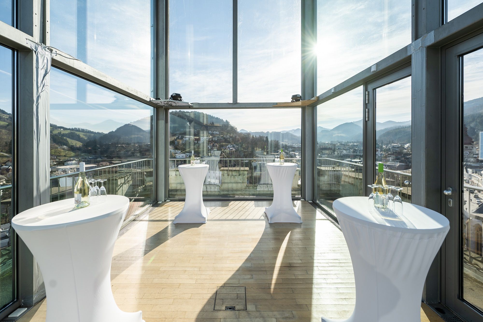 Innenansicht eines modernen Glasraums mit Stehtischen und Bergblick.